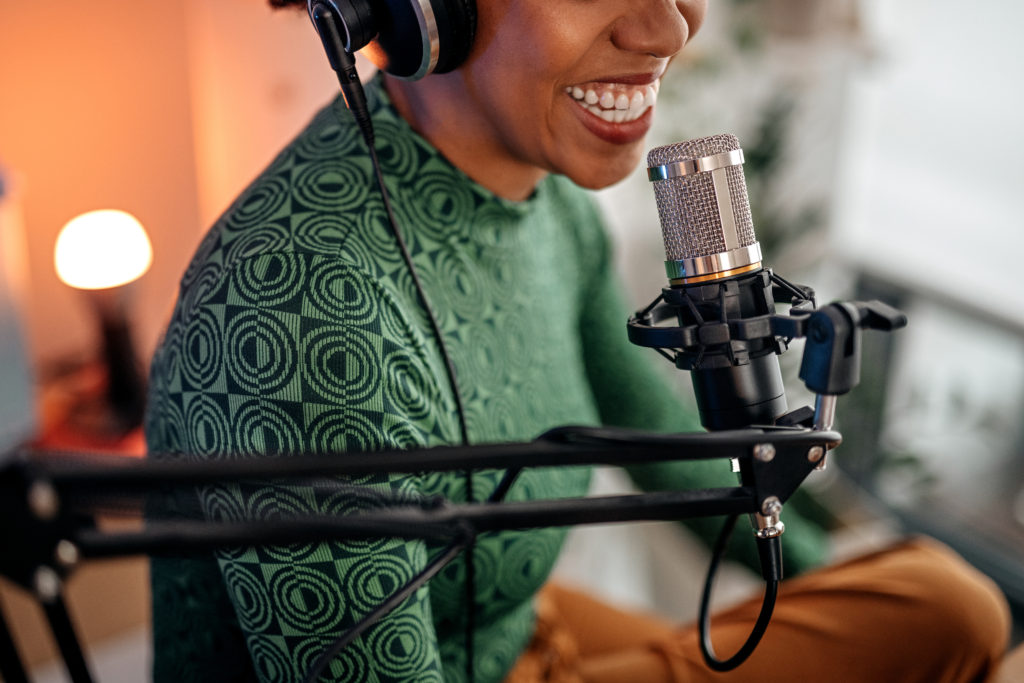 Selective focus of mouth of young smiling women recording podcast and doing live streaming using microphone and headphones in recording studio